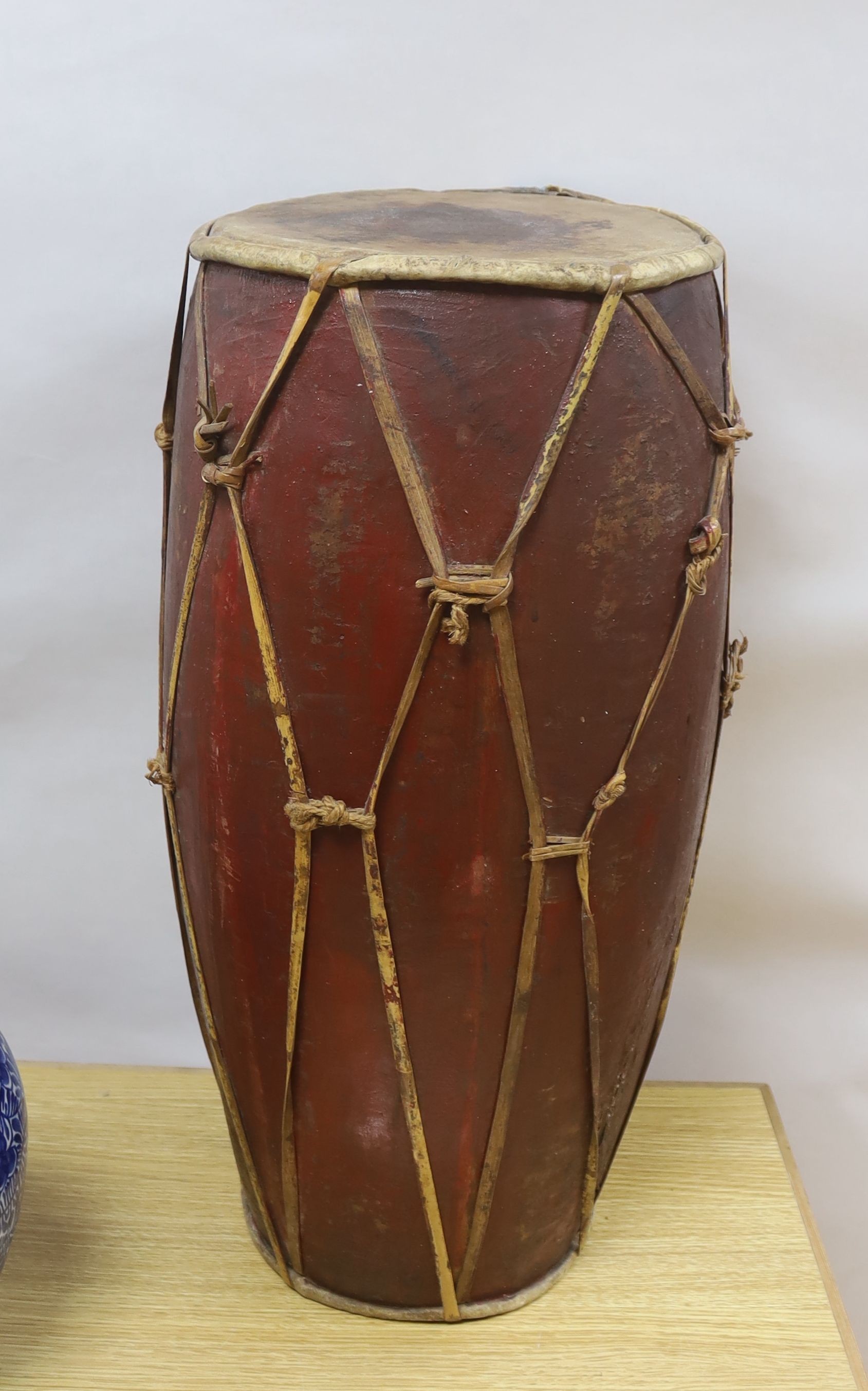 A tall tribal wooden drum, the vellum skins held by bamboo strapping and decorated in red and ochre - 62cm